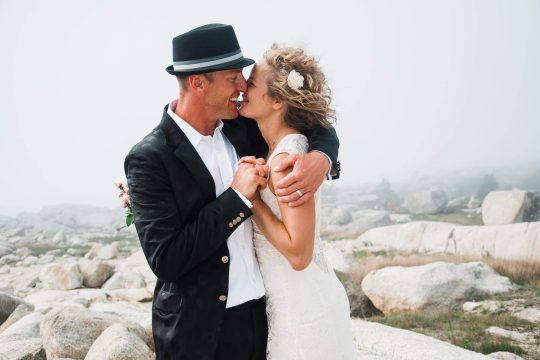 newlywed couple hugging and laughing near the ocean