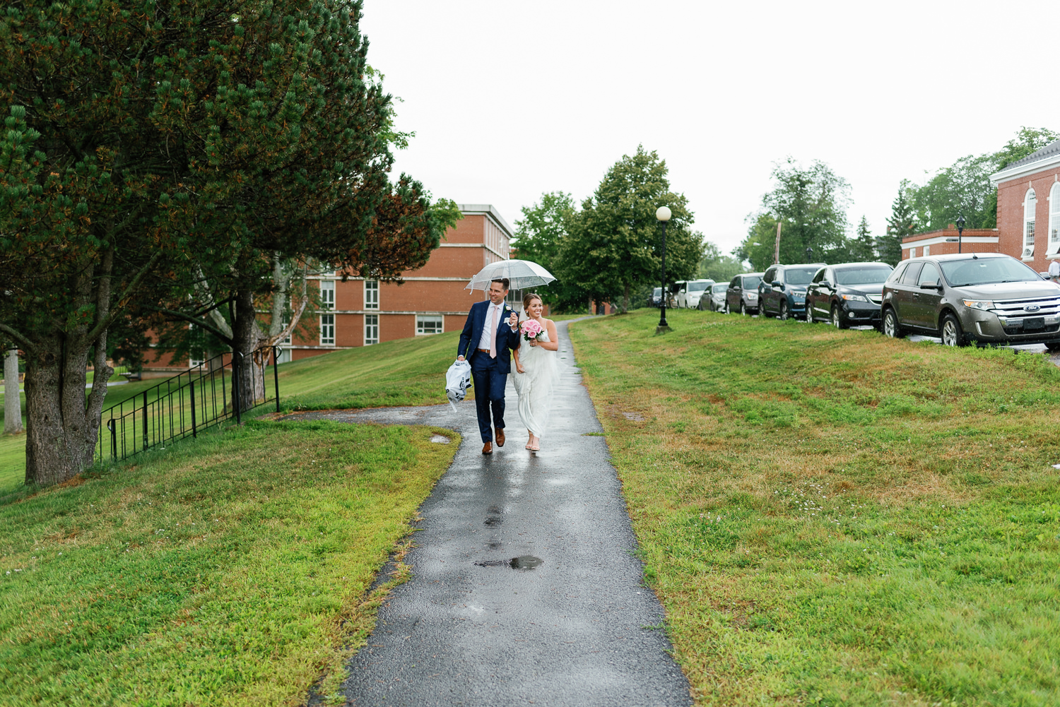 bride and groom walk in the rain around acadia university campus