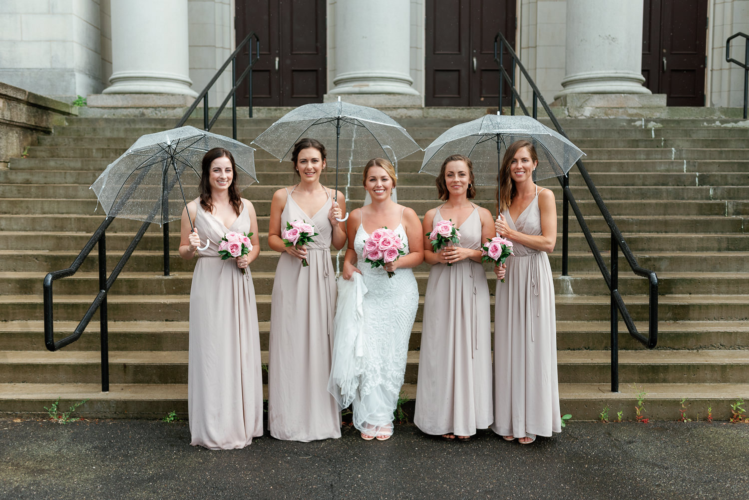 bride and bridesmaids pose in the rain around acadia university campus