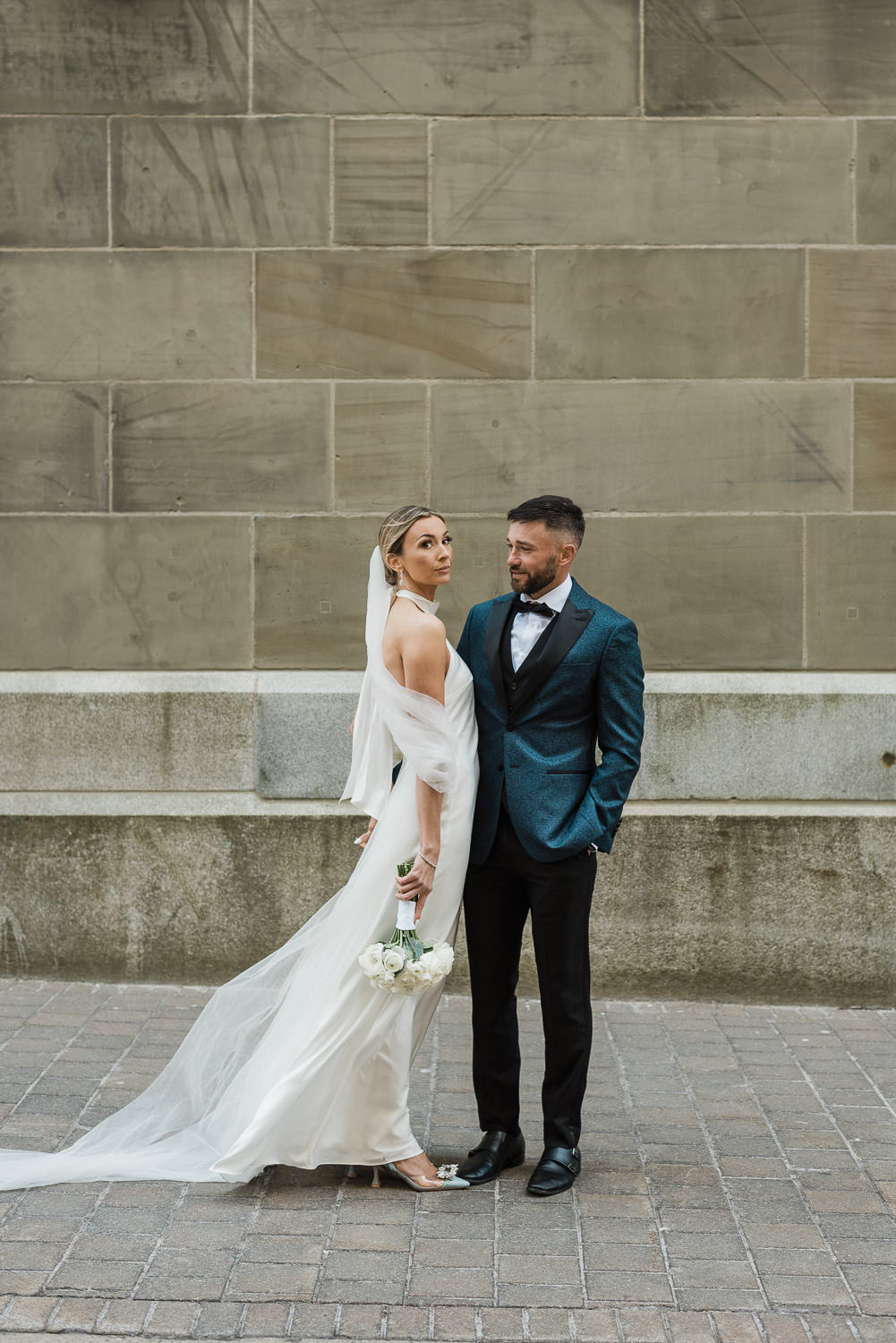 Bride and groom pose in front of beige stone brick building in downtown Halifax