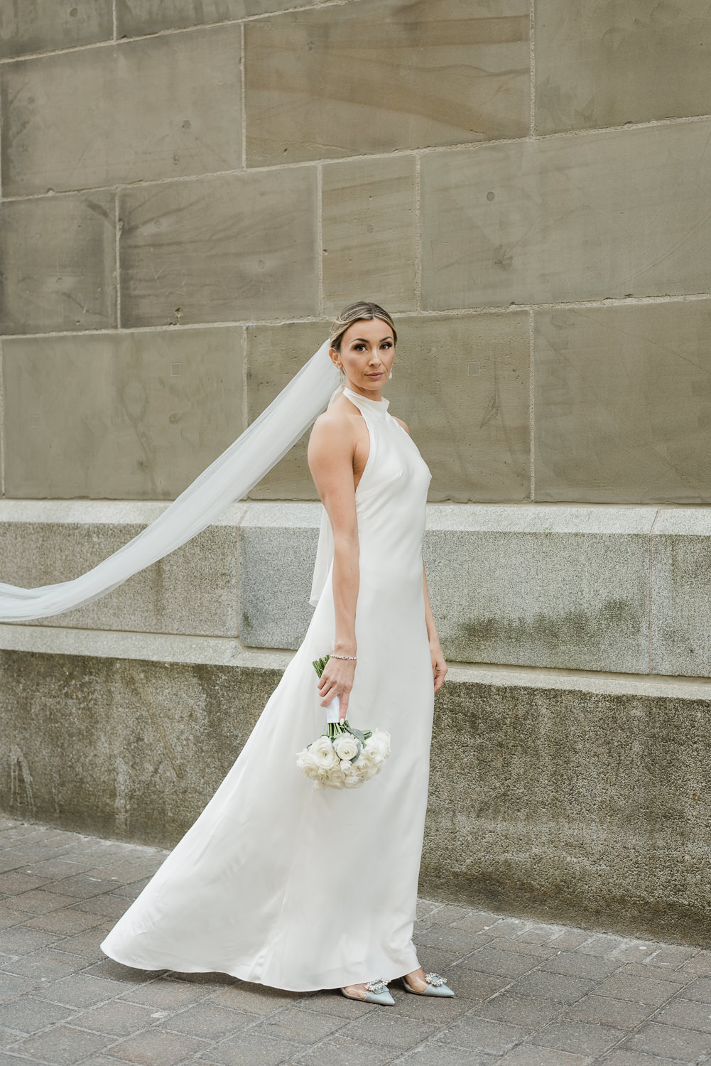 Stylish bride poses in front of beige stone building in downtown Halifax