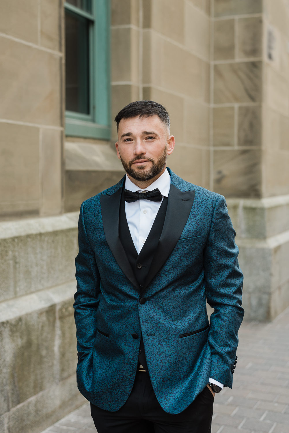 Stylish groom poses in front of beige stone building in downtown Halifax