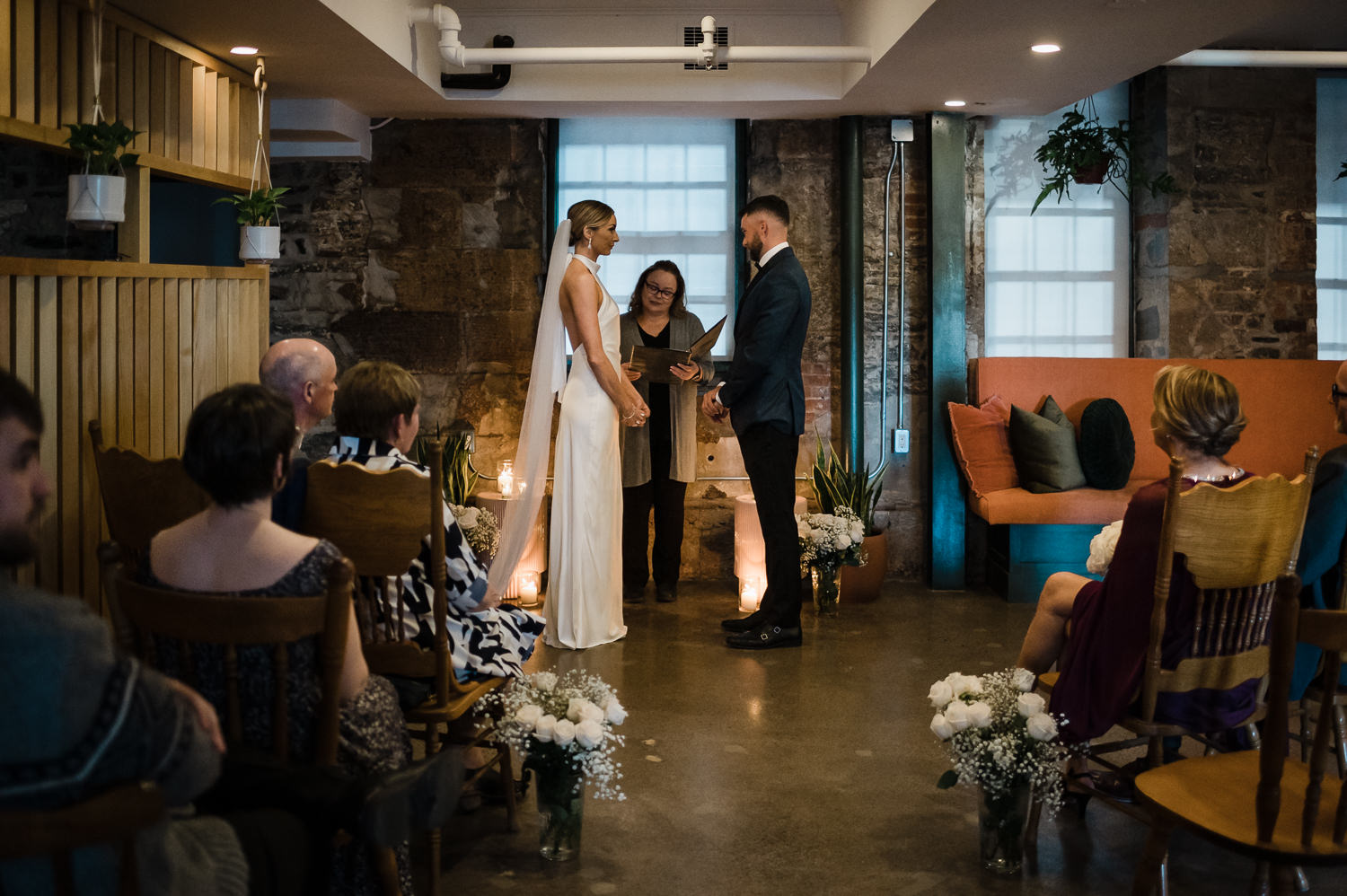 Bride and groom stand together while family watches them get married during ceremony at Anemone Dining