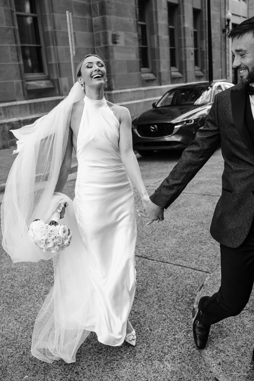 Bride and groom laugh joyfully as they cross the street in downtown Halifax