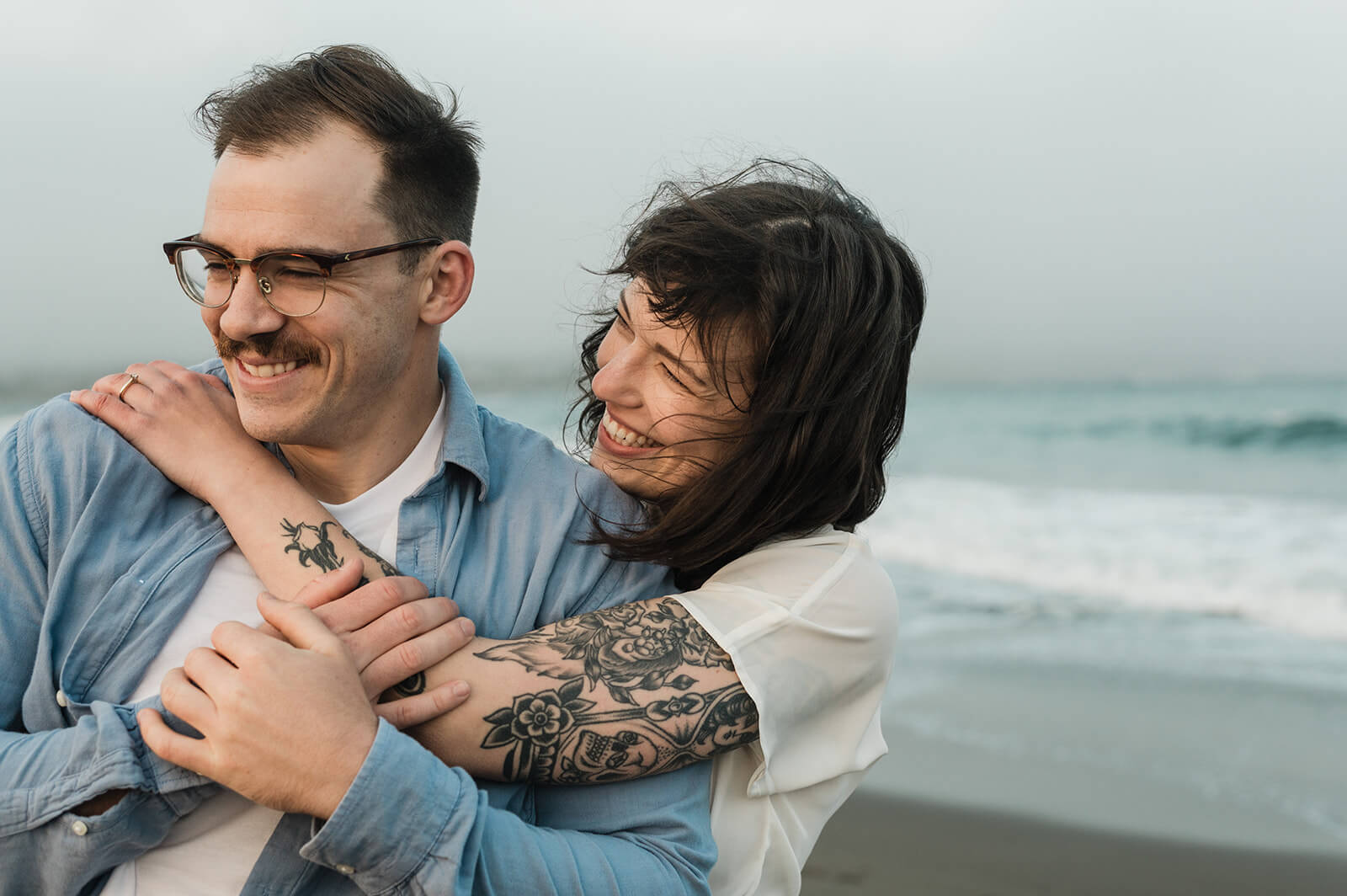 couple laugh during engagement session at rainbow haven beach