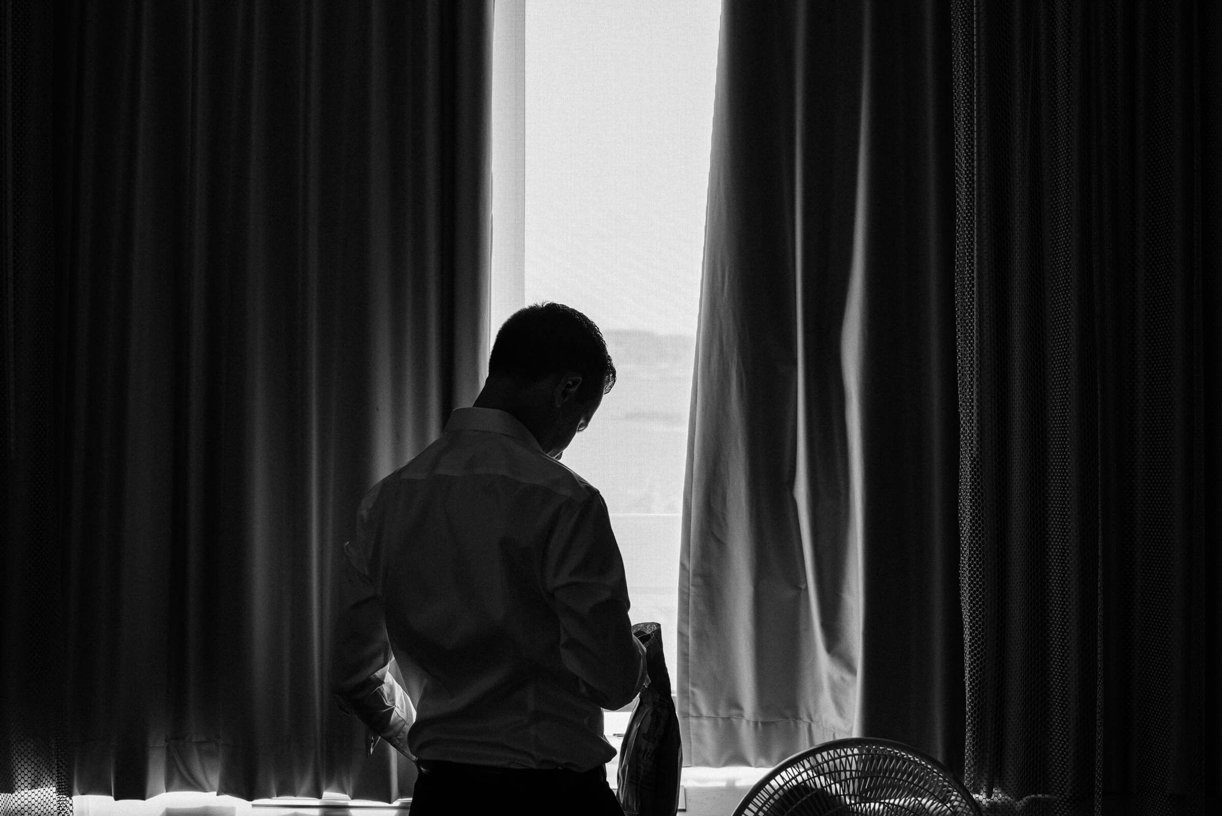 groom gets ready for window against backlit window 